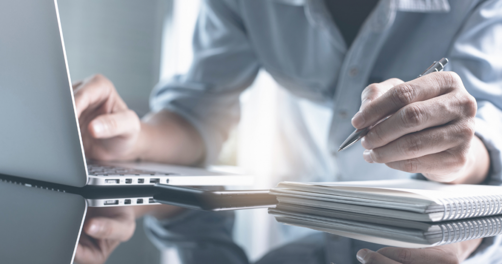 Homem mexendo num notebook e fazendo anotações para capacitação em ouvidoria